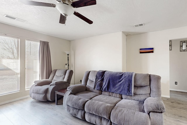 living room featuring light hardwood / wood-style flooring, ceiling fan, and a textured ceiling
