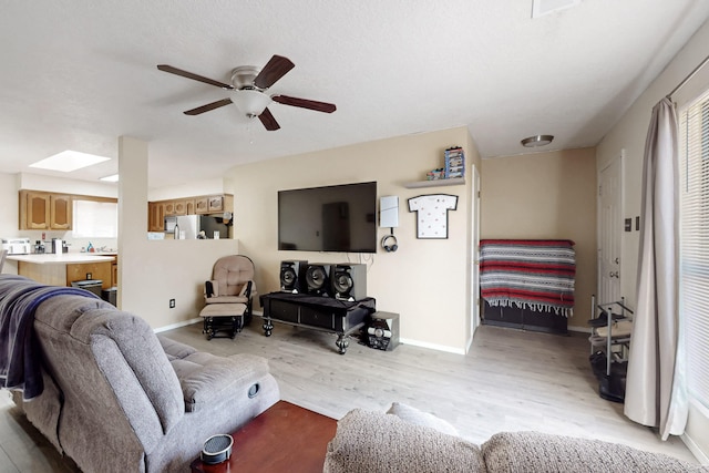 living room featuring ceiling fan, light wood-type flooring, and a skylight