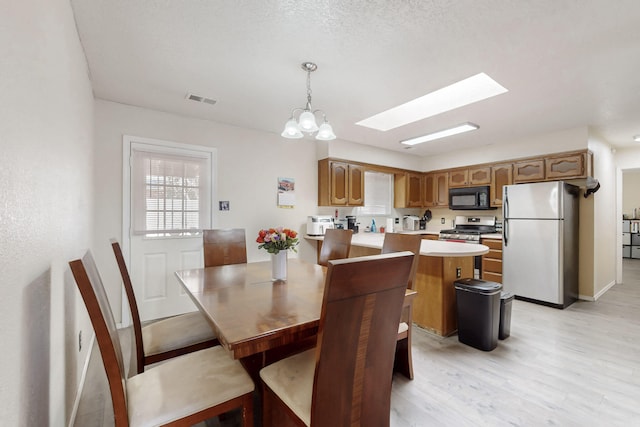 dining area featuring light hardwood / wood-style flooring, an inviting chandelier, a textured ceiling, and a skylight
