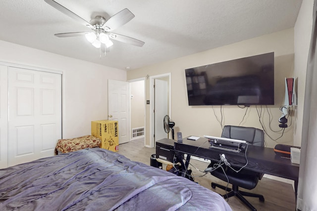 bedroom with ceiling fan, light hardwood / wood-style flooring, a textured ceiling, and a closet