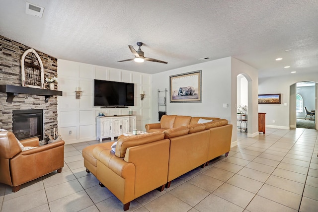 living area with light tile patterned floors, a textured ceiling, arched walkways, a fireplace, and visible vents