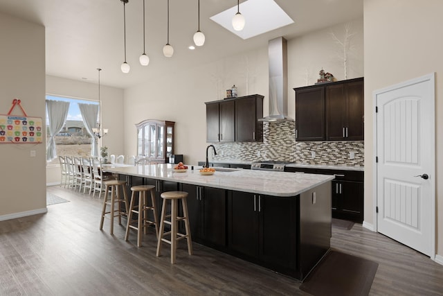 kitchen featuring a center island with sink, sink, pendant lighting, and wall chimney range hood