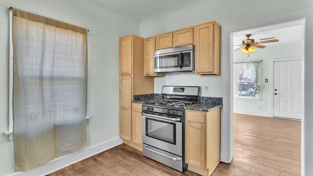 kitchen featuring dark stone counters, appliances with stainless steel finishes, light brown cabinets, and light wood-style floors