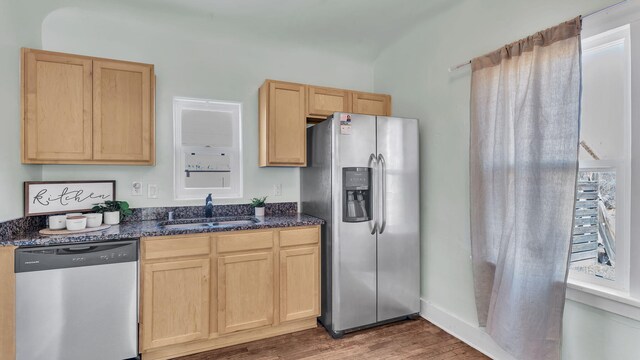 kitchen featuring stainless steel appliances, dark stone counters, a sink, and light brown cabinetry