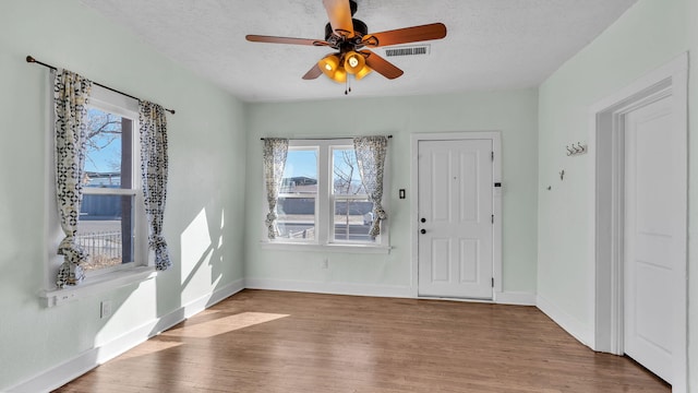 foyer entrance with visible vents, baseboards, a ceiling fan, wood finished floors, and a textured ceiling