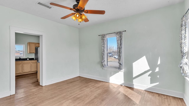 empty room featuring light wood-style flooring, visible vents, baseboards, and ceiling fan