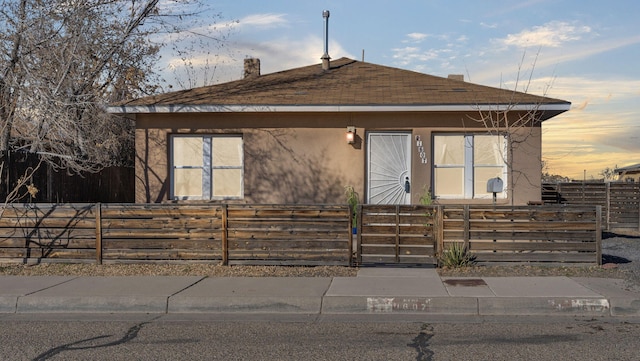 view of front of house featuring roof with shingles, a fenced front yard, and stucco siding