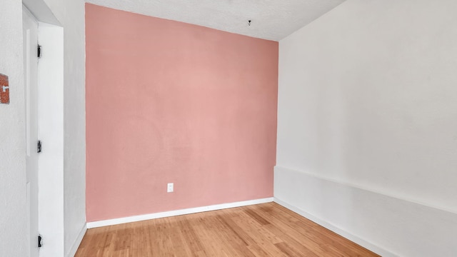 spare room featuring a textured ceiling, baseboards, and wood finished floors