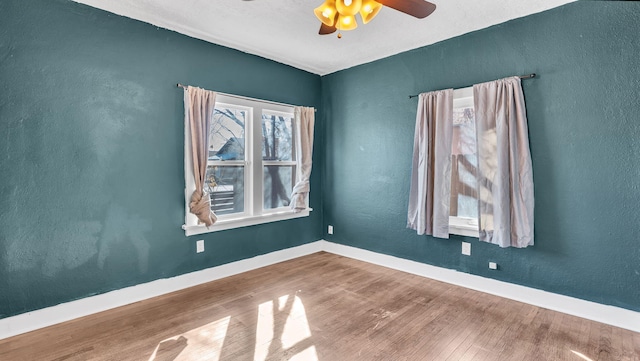 unfurnished room with a textured wall, ceiling fan, baseboards, and wood finished floors