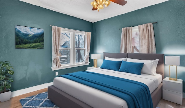 bedroom with a ceiling fan, baseboards, wood finished floors, and a textured wall