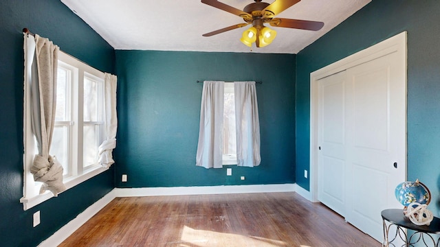 unfurnished bedroom featuring a closet, wood finished floors, a ceiling fan, and baseboards