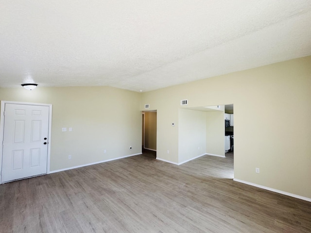 empty room featuring a textured ceiling, wood finished floors, visible vents, and baseboards