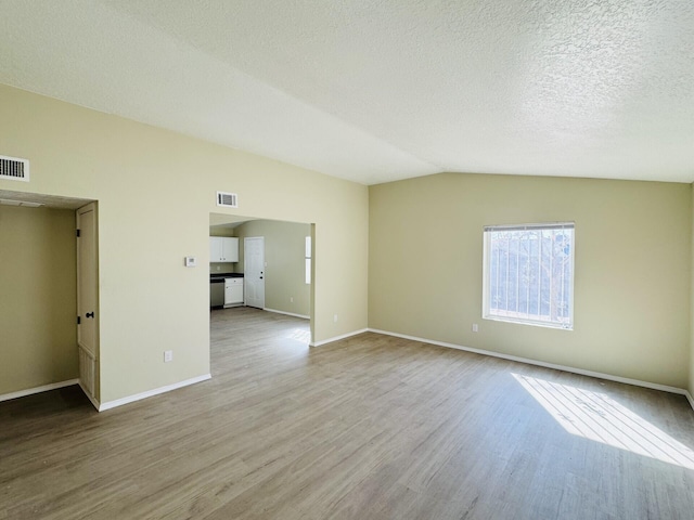 empty room with a textured ceiling, wood finished floors, visible vents, baseboards, and vaulted ceiling