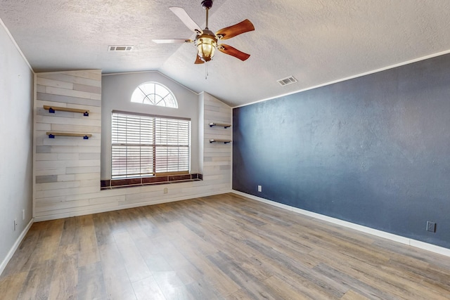 empty room with a ceiling fan, visible vents, vaulted ceiling, and wood finished floors