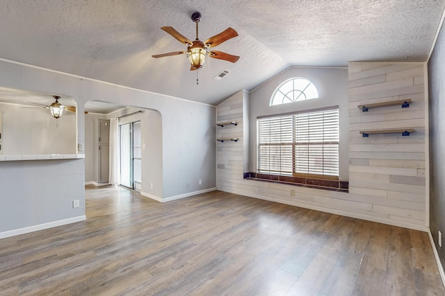 unfurnished room featuring arched walkways, ceiling fan, a textured ceiling, wood finished floors, and vaulted ceiling