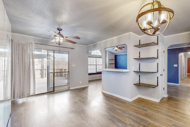 unfurnished living room with ceiling fan with notable chandelier, arched walkways, crown molding, and wood finished floors