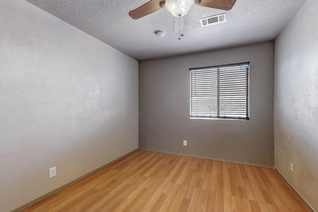 unfurnished room featuring a ceiling fan, visible vents, light wood-style flooring, and a textured ceiling