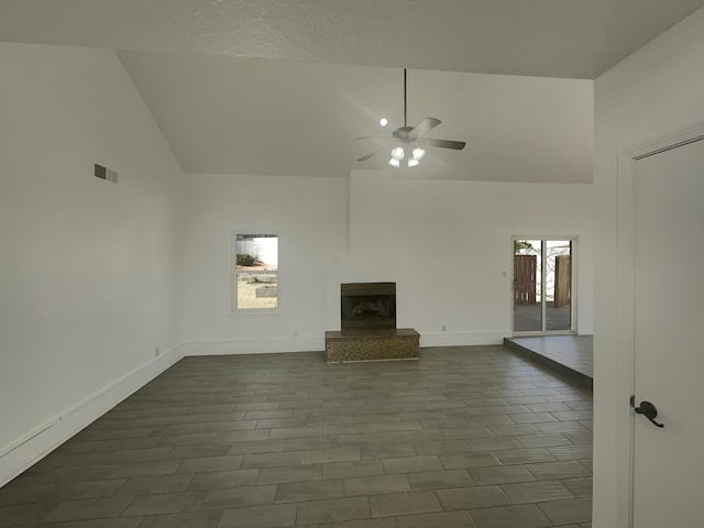 unfurnished living room featuring a fireplace with raised hearth, visible vents, baseboards, high vaulted ceiling, and ceiling fan