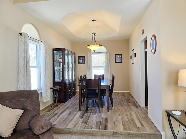 dining space featuring light wood finished floors, a raised ceiling, and baseboards