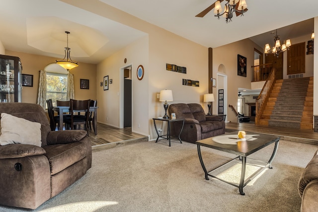 carpeted living room with baseboards, arched walkways, stairs, a tray ceiling, and ceiling fan with notable chandelier