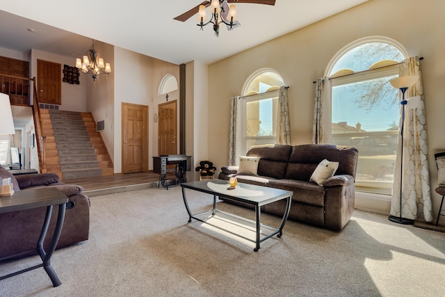 living room with ceiling fan with notable chandelier, stairway, and light colored carpet