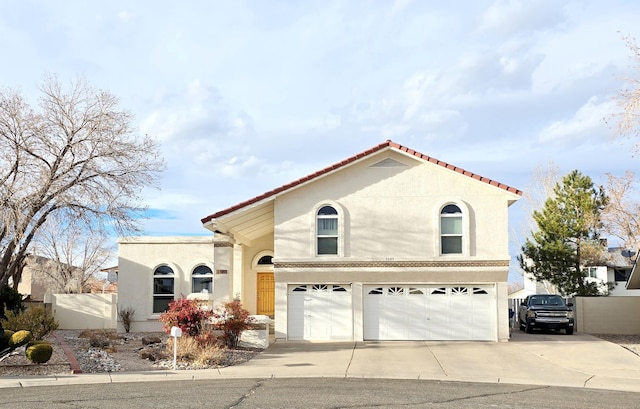 mediterranean / spanish house with an attached garage, fence, concrete driveway, and stucco siding