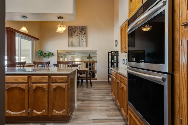 kitchen featuring light wood-type flooring, brown cabinets, stainless steel double oven, and decorative light fixtures