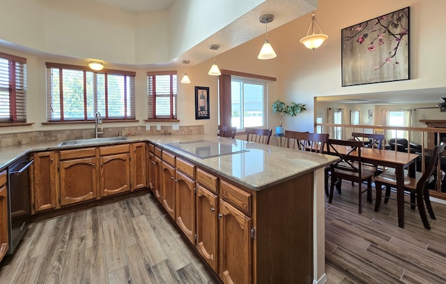 kitchen with black electric cooktop, a peninsula, a sink, hanging light fixtures, and dishwasher