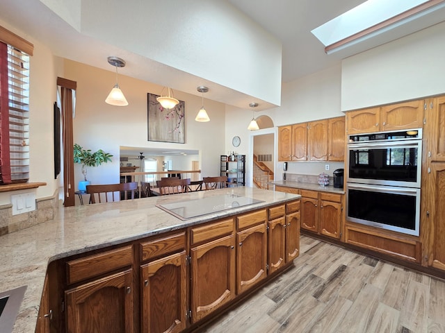 kitchen featuring a skylight, brown cabinets, hanging light fixtures, a peninsula, and stainless steel double oven