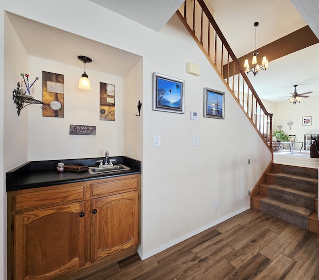 bar featuring dark wood-style floors, pendant lighting, a sink, and stairs