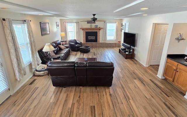 living room featuring a fireplace, visible vents, light wood-style flooring, ceiling fan, and a textured ceiling