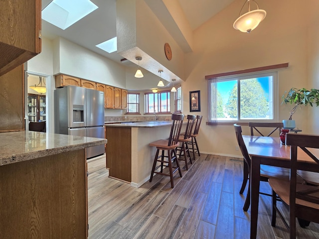 kitchen featuring a peninsula, stainless steel refrigerator with ice dispenser, a skylight, and pendant lighting