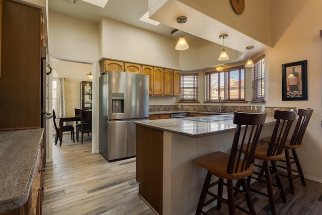 kitchen featuring a skylight, brown cabinetry, appliances with stainless steel finishes, a center island, and hanging light fixtures