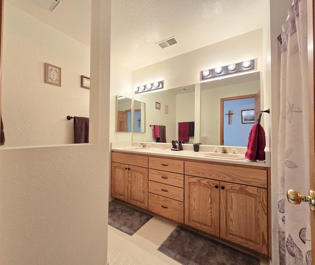 bathroom with double vanity, visible vents, a sink, and a textured wall