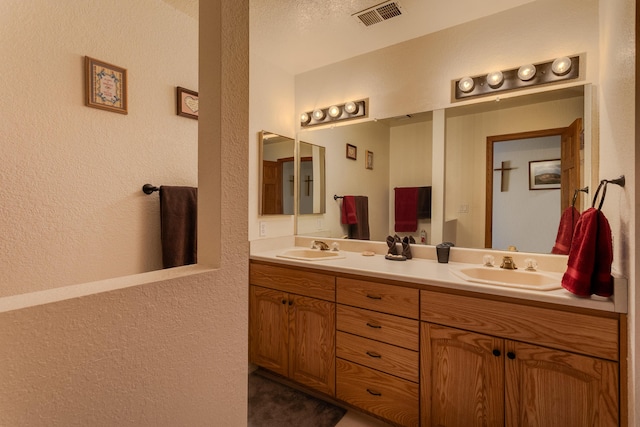 bathroom featuring a textured wall, visible vents, a sink, and double vanity