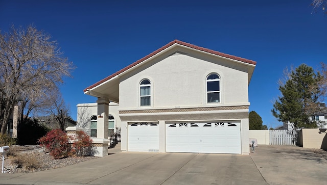 traditional-style home with concrete driveway, a tiled roof, an attached garage, fence, and stucco siding