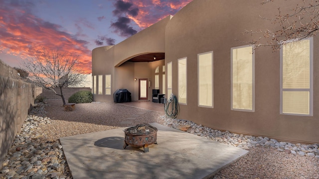 property exterior at dusk with a fire pit, a fenced backyard, a patio, and stucco siding