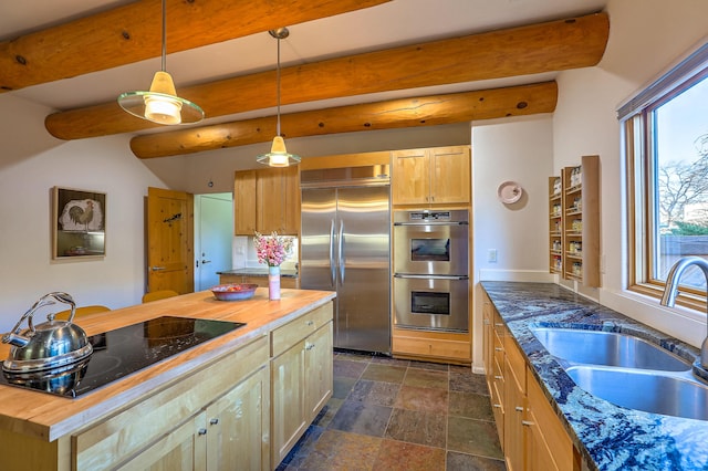 kitchen featuring butcher block countertops, a sink, appliances with stainless steel finishes, beam ceiling, and stone finish floor