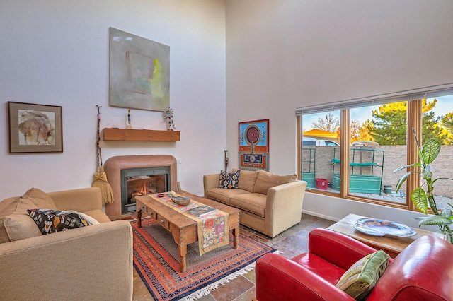 living area with a warm lit fireplace, stone finish flooring, a high ceiling, and baseboards