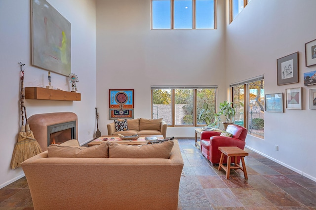 living area featuring a warm lit fireplace, a high ceiling, stone tile floors, and baseboards