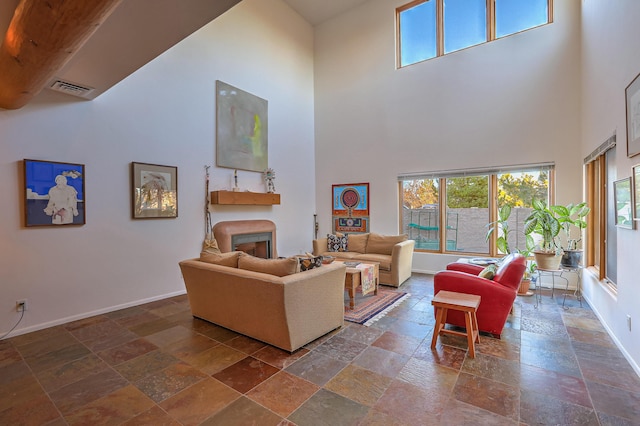 living room with a high ceiling, a fireplace, visible vents, baseboards, and stone tile flooring