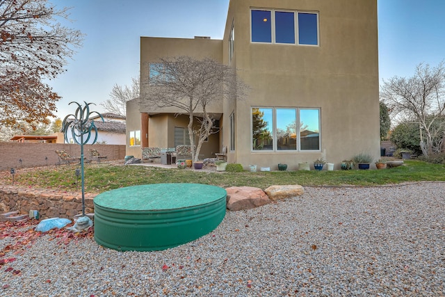 rear view of property with a lawn, fence, and stucco siding