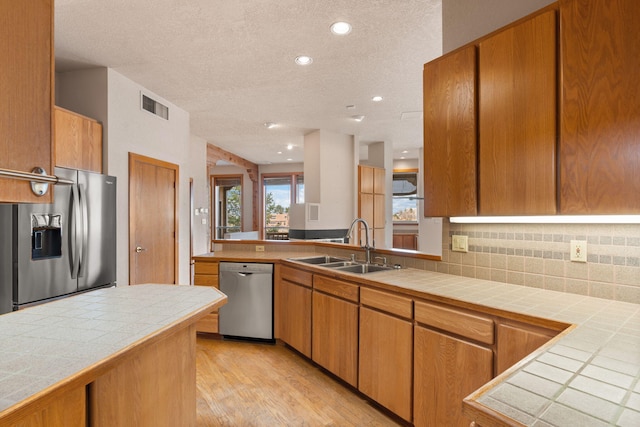 kitchen featuring a sink, visible vents, appliances with stainless steel finishes, tile counters, and brown cabinetry