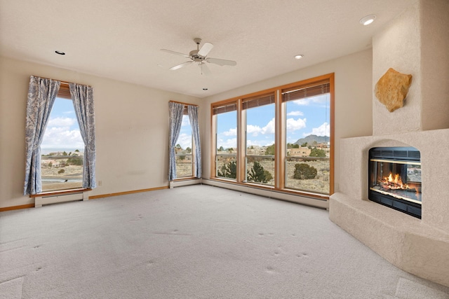 unfurnished living room with carpet floors, a baseboard heating unit, a glass covered fireplace, a ceiling fan, and baseboards