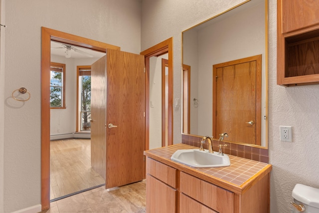 bathroom with a textured wall, baseboard heating, toilet, vanity, and tile patterned flooring