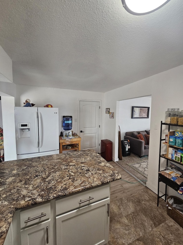 kitchen with white refrigerator with ice dispenser, open floor plan, dark stone countertops, and a textured ceiling