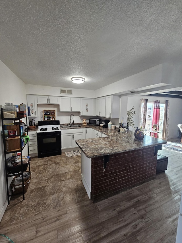 kitchen featuring a peninsula, dark wood-style flooring, visible vents, white cabinets, and range with gas stovetop