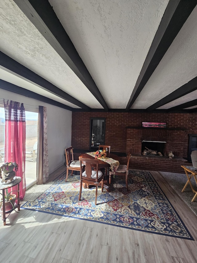 dining space with a textured ceiling, brick wall, beamed ceiling, and a fireplace