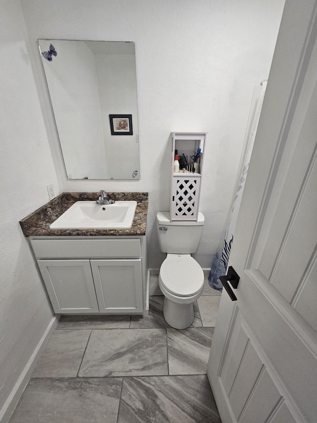 bathroom featuring toilet, marble finish floor, vanity, and baseboards