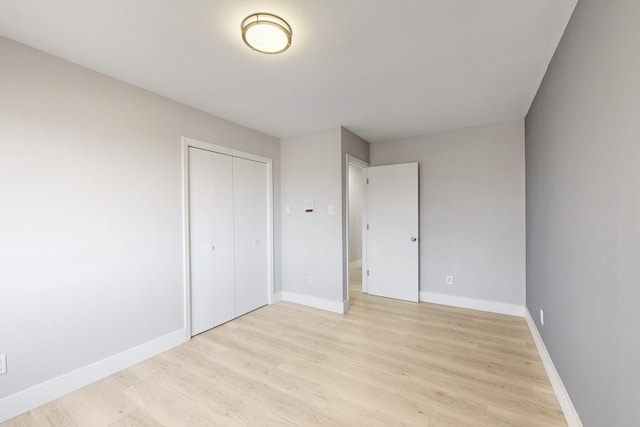 unfurnished bedroom featuring light wood finished floors, baseboards, and a closet